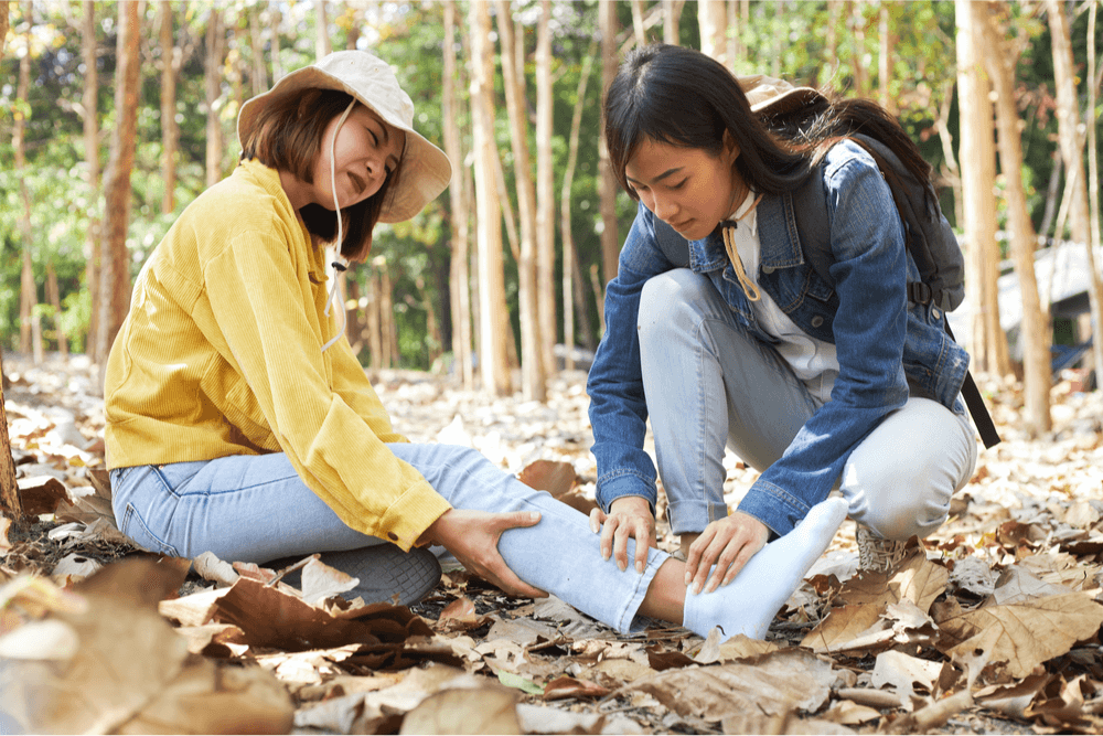 Asian woman helping her friend with a sprained ankle in a forest