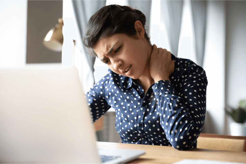 Woman frowning at her laptop while massaging her shoulders at a desk