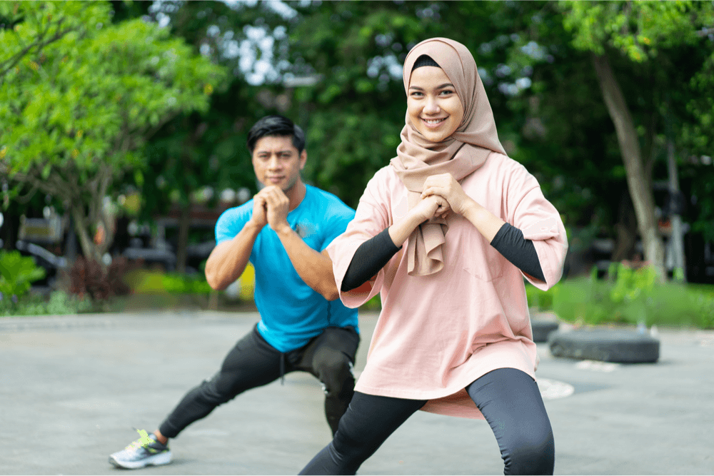 Two women wearing hijab stretching their legs in a park as a warm-up exercise