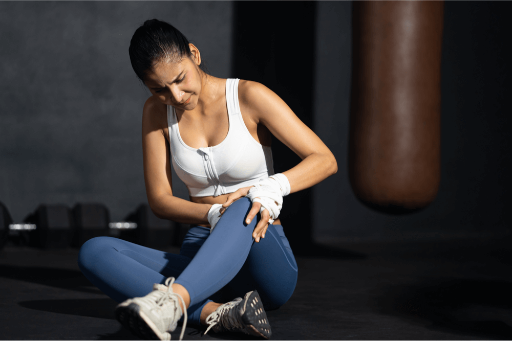 Young Asian woman experiencing painful knee muscle injury after workout